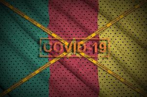 Cameroon flag and Covid-19 stamp with orange quarantine border tape cross. Coronavirus or 2019-nCov virus concept photo