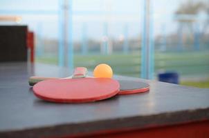 raquetas y pelota en la mesa de ping pong en el patio deportivo al aire libre. concepto de deporte activo y entrenamiento físico foto