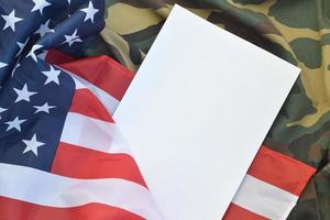 Blank paper lies on United States of America flag and folded military uniform jacket. Military symbols conceptual background banner and copy space photo