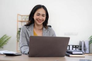retrato de una mujer de negocios joven asiática que trabaja en una computadora portátil en su estación de trabajo. concepto de marketing de informe en línea independiente de empleados de negocios. foto