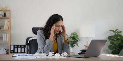 Tired business woman in stress works at a laptop while sitting at a table at home and holds her hand on her temples, migraine attack. Freelance, work from home. photo