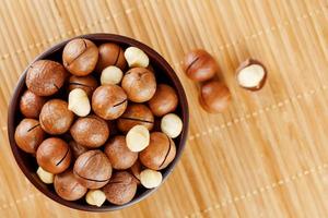 Macadamia nut on bamboo texture in a wooden cup, peeled and not peeled walnut, top view photo