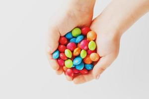 Multicolored candies in the hands of a child on a white isolated background. Low contrast photo