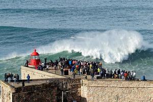 Nazare, Portugal - November 7, 2022 People watching the big giant waves crashing near the Fort of Nazare Lighthouse in Nazare, Portugal. Biggest waves in the world. Touristic destination for surfing.