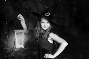 Halloween concept.A teenage girl in a witch costume and a lantern in her hands for Halloween. Black and white photo