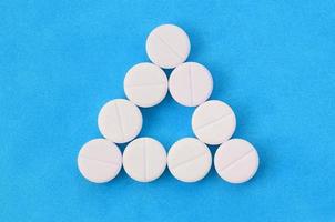 Several white tablets lie on a bright blue background in the form of an even triangle. Background image on medicine and pharmaceutical topics photo