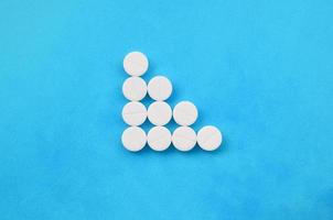 Several white tablets lie on a bright blue background in the form of a triangular arrow. Background image on medicine and pharmaceutical topics photo