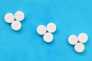 Several white tablets lie on a bright blue background in the form of three triangular arrows. Background image on medicine and pharmaceutical topics photo