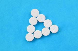 Several white tablets lie on a bright blue background in the form of an even triangle. Background image on medicine and pharmaceutical topics photo