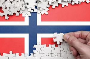 Norway flag  is depicted on a table on which the human hand folds a puzzle of white color photo