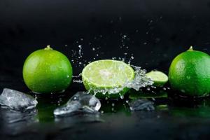 Water drops on lemon slices and splash with ice cubes on table on black background. selective focus.
