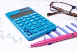 Business financial report background. Calculator, pen, eyeglasses and charts on work desk photo