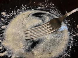 tenedor en un plato oscuro vacío con algo de comida sobrante. plato sucio después de la cena. foto