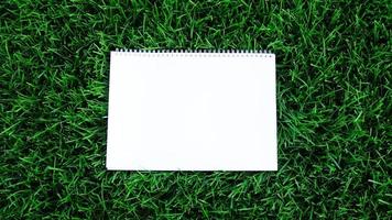 Empty white paper on green grass background. For message flat lay with copy space for text or products presentation. Nature concept, business and lifestyle environment. photo