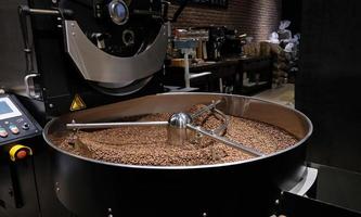 máquina tostadora de café en el proceso de tostado de café. mezclando granos de café. Máquinas profesionales de enfriador giratorio asado y foto oscura de primer plano de movimiento de granos de café marrón fresco en la fábrica.