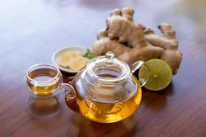 a cup of tea with ginger root, lime, cinnamon and teapot on wooden background. Health drink concept. photo