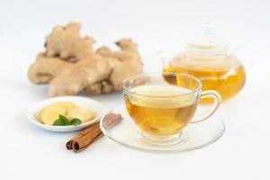 a cup of tea with ginger root, lime, cinnamon and teapot on white background. Health drink concept. photo