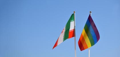 Iran national flag and rainbow flag stand together against bluesky background, concept for lgbt celebration and respecting gender diversity of human in Iran, soft and selective focus. photo