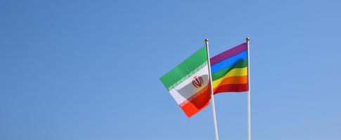 Iran national flag and rainbow flag stand together against bluesky background, concept for lgbt celebration and respecting gender diversity of human in Iran, soft and selective focus. photo