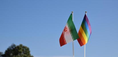 Iran national flag and rainbow flag stand together against bluesky background, concept for lgbt celebration and respecting gender diversity of human in Iran, soft and selective focus. photo