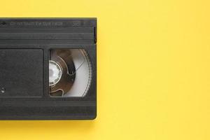 Black VHS videotape recorder cassette on yellow background. Old obsolete technology for tape recording and watching media movies. Retro, vintage, history, nostalgia concept. Flat lay, copy space photo