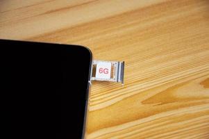 G technology, Internet concept. SIM card in smartphone tray on wooden table, closeup 6G network concept, high speed mobile internet New age network, business concept photo