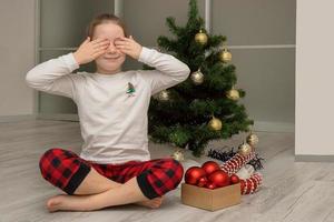 chica en pijama cerró los ojos sentada junto al árbol de navidad, vacaciones de invierno foto