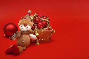 snowman next to Christmas balls and toys on a red background with copy space, Christmas card photo