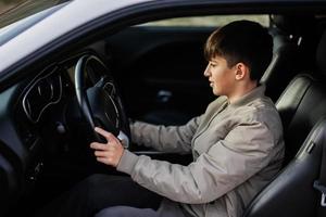 Teenager boy sit in muscle car. Young teen driver. photo