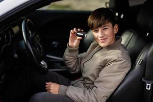 Teenager boy sit in muscle car. Young teen driver showing keys. photo