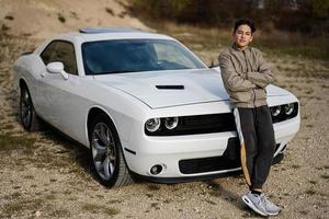 Teenager boy stand near white muscle car. Young teen driver. photo