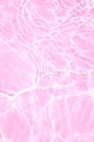 desenfoque borroso transparente color rosa claro agua tranquila textura superficial con salpicaduras y burbujas. fondo de naturaleza abstracta de moda. ondas de agua a la luz del sol con espacio de copia. brillo de color de agua rosa foto