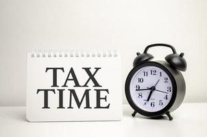 Tax Time typography text on paper card with alarm clock and calculator on white background