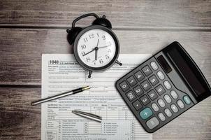 1040 US individual tax form, calculator, black clock and wooden background photo