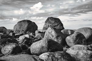 Big stones in black and white taken on stone beach in front of sea with clouds in sky