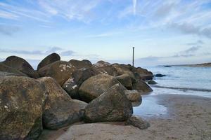 Stone groyne juts out into the water off the coast in Denmark. Sunny day. Landscape photo