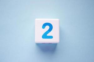 Close-up photo of a white plastic cube with a blue number 2 on a blue background. Object in the center of the photo