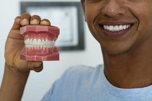 Close-up cropped image of a young man showing a mock-up of teeth. photo