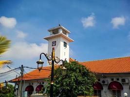 Big wall clock in an old white building in Madiun, East Java, Indonesia, with a beautiful bright blue sky. photo