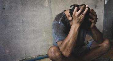 Drugs addiction and withdrawal symptoms concept. Depressed and hopeless man sitting alone after using drugs and drunk alcohol at abandoned house. homeless,  International Day against Drug Abuse. photo