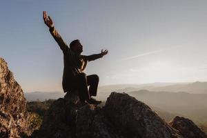 silhouette of man rise hand up praying  on top of mountain and sunset sky abstract background. Freedom and travel adventure concept. photo