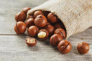 Macadamia nuts spilled out of the bag on a wooden background close-up with one peeled nut photo