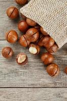 Macadamia nuts spilled out of the bag on a wooden background close-up with one peeled nut photo