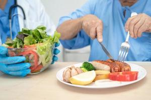 Asian senior or elderly old lady woman patient eating breakfast and vegetable healthy food with hope and happy while sitting and hungry on bed in hospital. photo