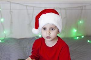 Portrait of a cute boy in a Santa Claus hat. Funny smiling child. Gifts, toys, joy, celebration. photo