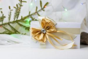 A Christmas gift decorated with a beautiful bow on a light background with a twig, if. Selective focus. the concept of Christmas and New Year. photo