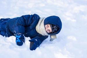 A smiling happy child lies in a snowdrift on a sunny winter day. A lot of snow and very frosty. Active winter outdoor games. photo