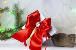 A Christmas gift decorated with a beautiful bow on a light background with a fir twig. Gifts, joy, surprise. Selective focus. the concept of Christmas and New Year. photo