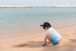 linda niña asiática jugando o haciendo castillos de arena o cavando con arena en una playa tropical. niños con hermoso mar, arena y cielo azul. niños felices de vacaciones en la playa corriendo en la playa. foto