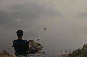 Rear view of young man sitting on folding chair by lake and fishing early in the morning photo